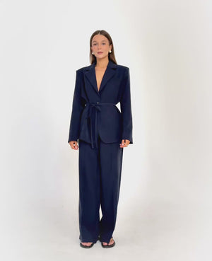 Granatowy garnitur dla niskich kobiet do 164 cm wzrostu – marynarka przewiązana w talii oraz eleganckie spodnie garniturowe z szeroką nogawką.